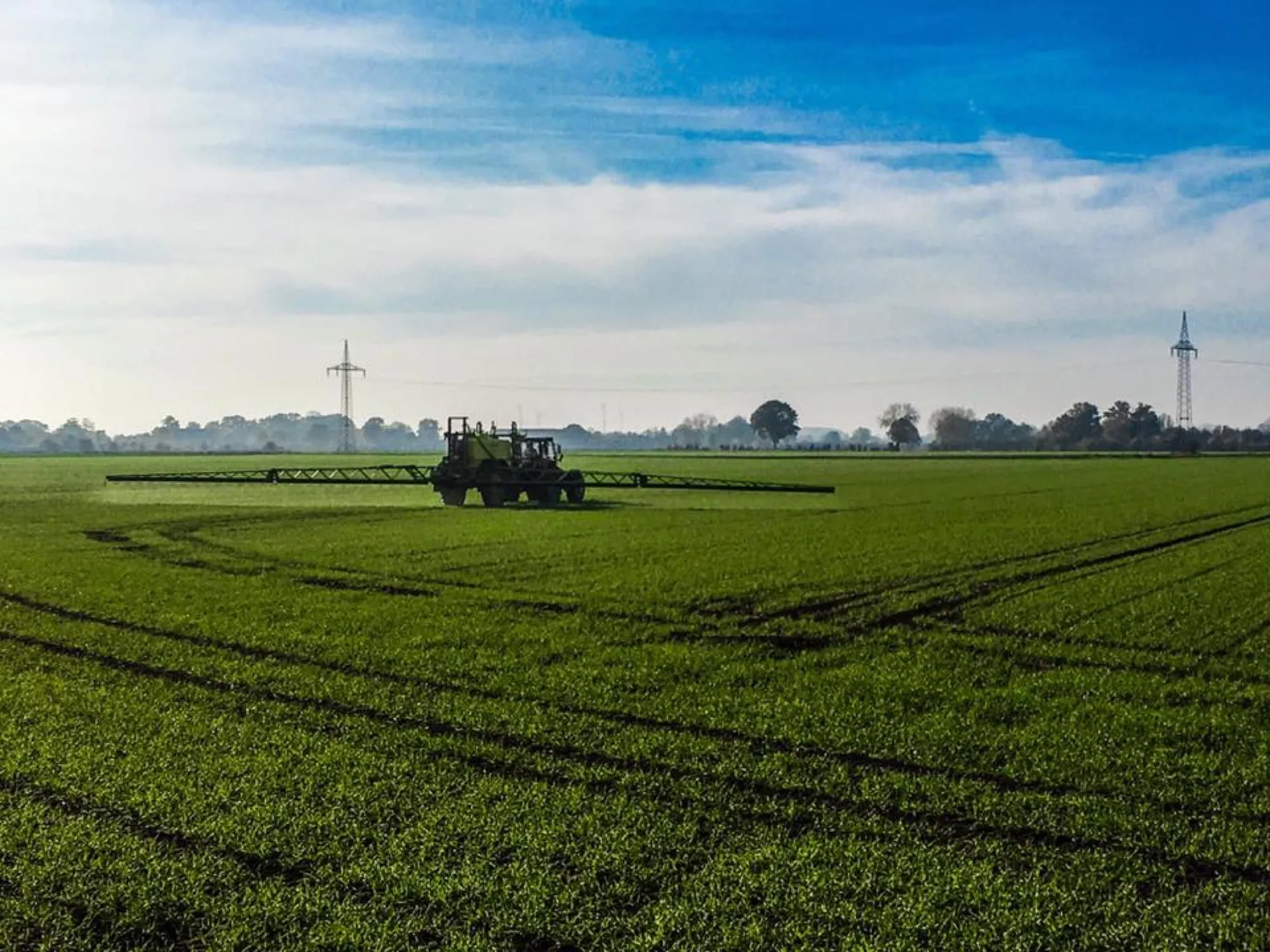 Feldarbeit im grünen Getreidebestand, Windräder am Horizont