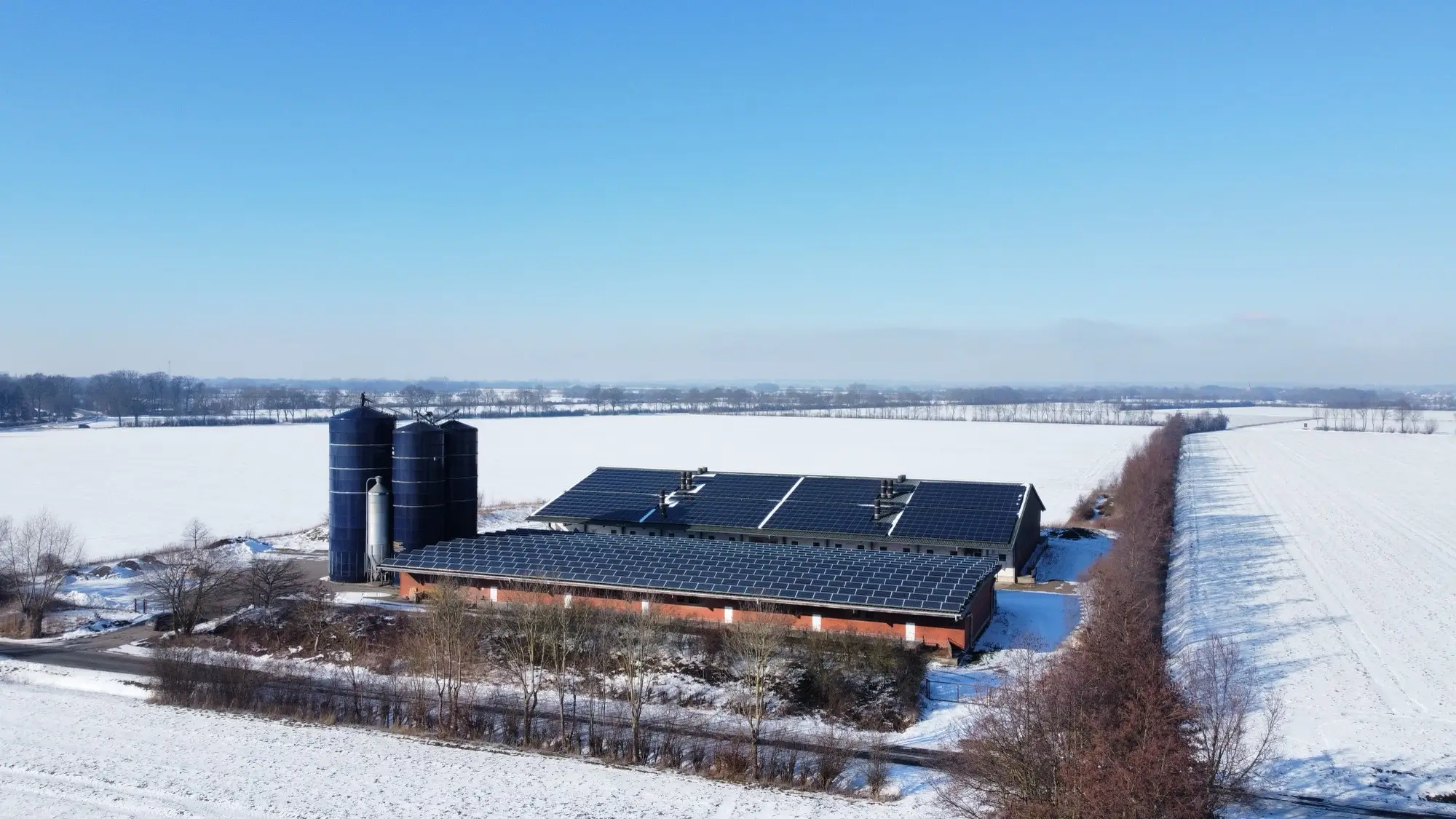 Luftaufnahme des Hofes im Winter, die Stalldächer vollständig mit Photovoltaik belegt